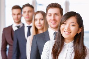 Team in the office. Businesswoman standing in the foreground smiling, her team of co-workers in the background