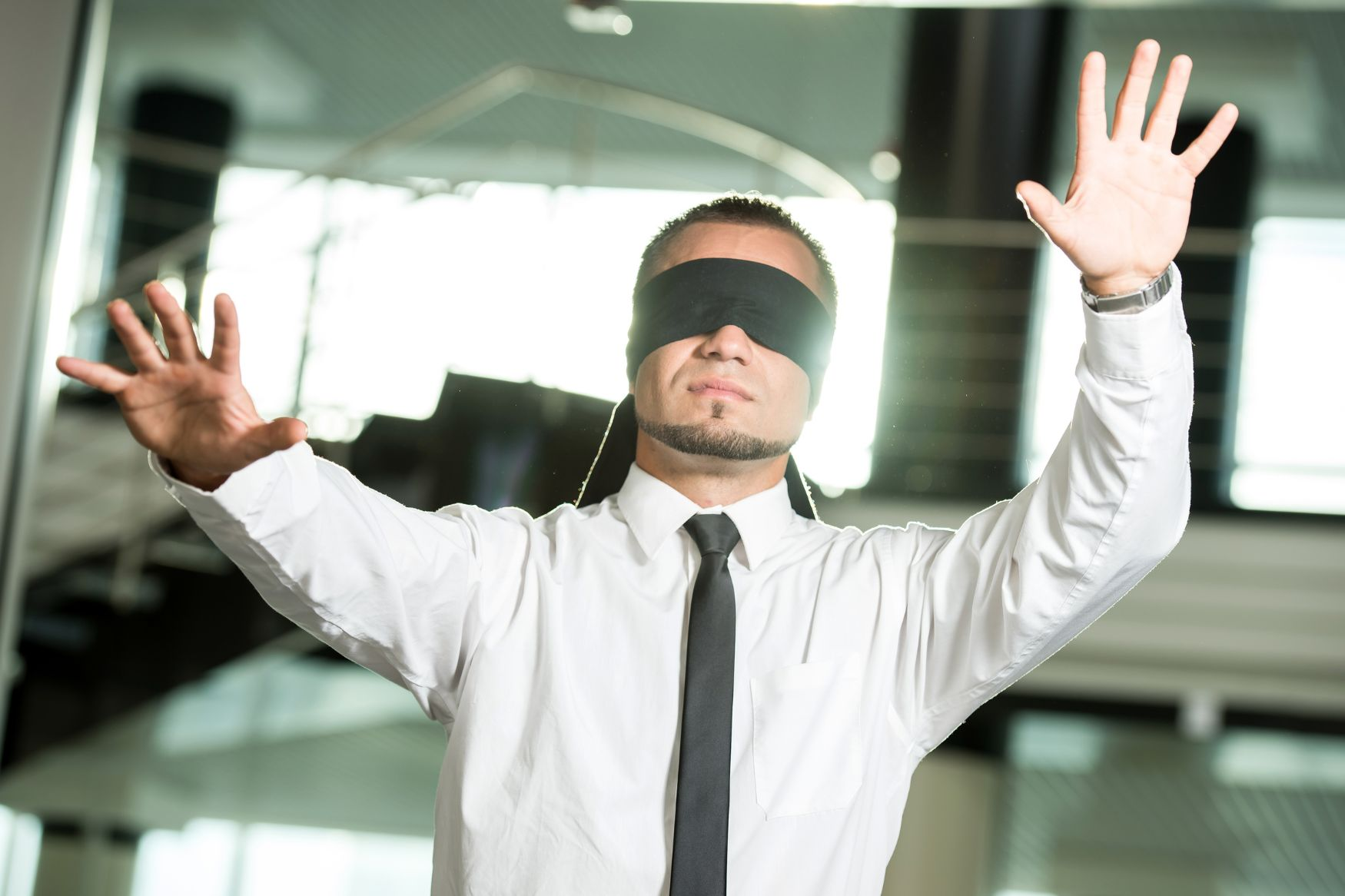 What We Don’t See: Uncovering Hidden Leadership Patterns A businessman in a white shirt and tie lifting a black blindfold to see clearly, symbolizing a leader uncovering hidden leadership patterns.